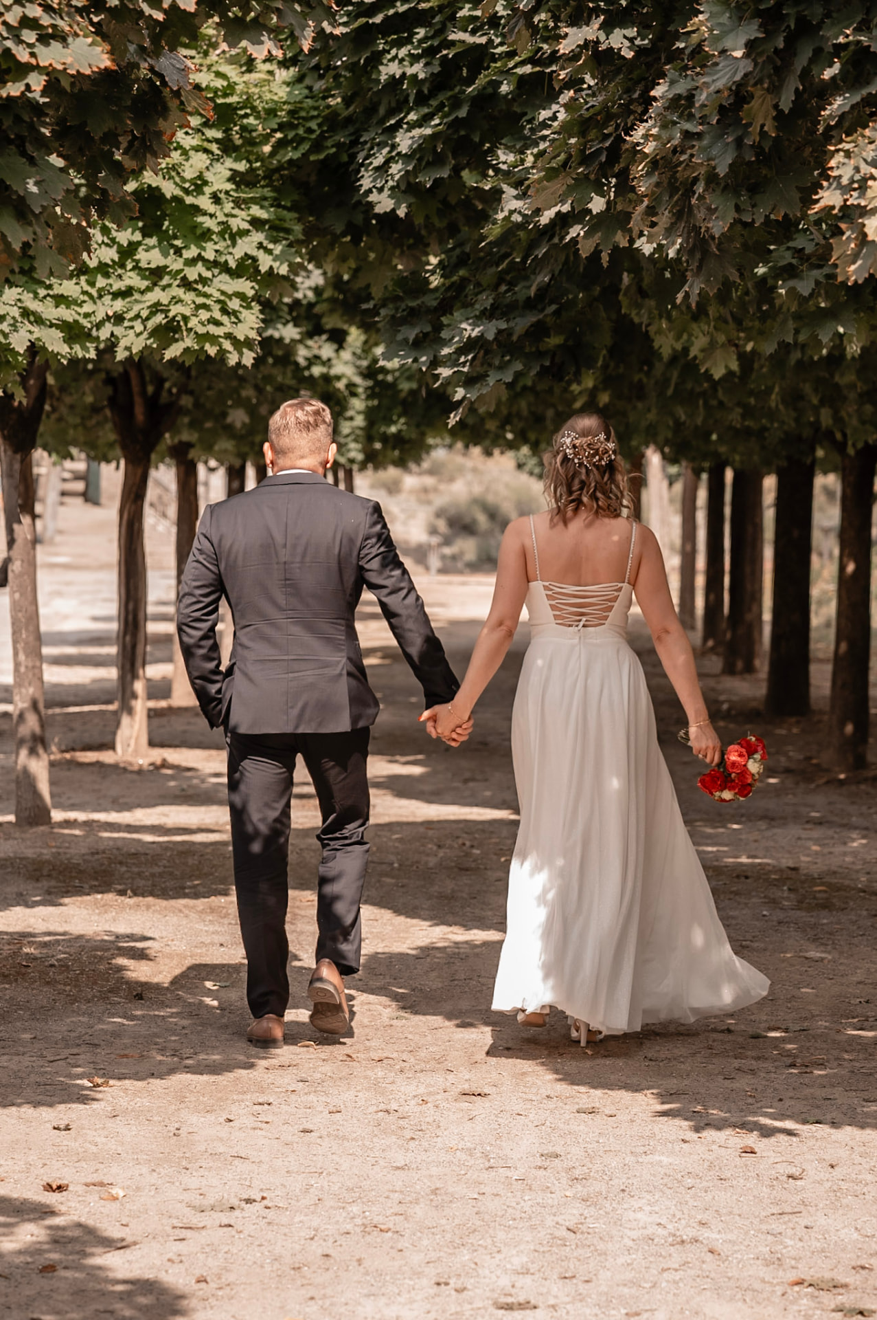 Brautpaar geht Hand in Hand durch eine Allee